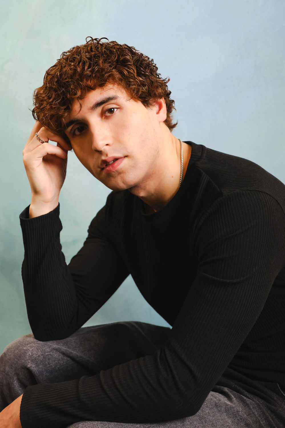 Relaxed actor portrait of a person seated in a natural pose against a soft mint backdrop, suited to contemporary casting.