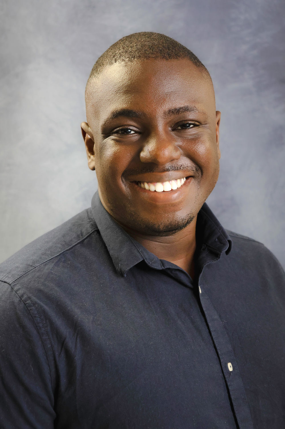 Professional headshot of a man in a dark shirt against a soft neutral background, suited to company team pages and business profiles.