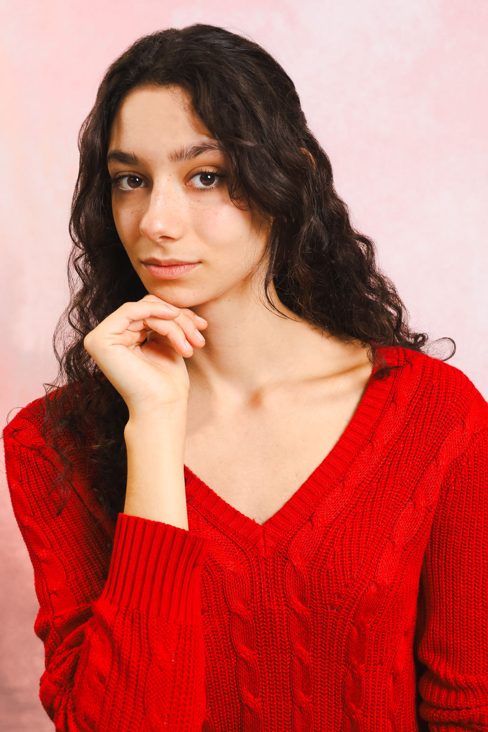 Casting-style actor headshot of a person resting a hand near their face against a soft pink backdrop.